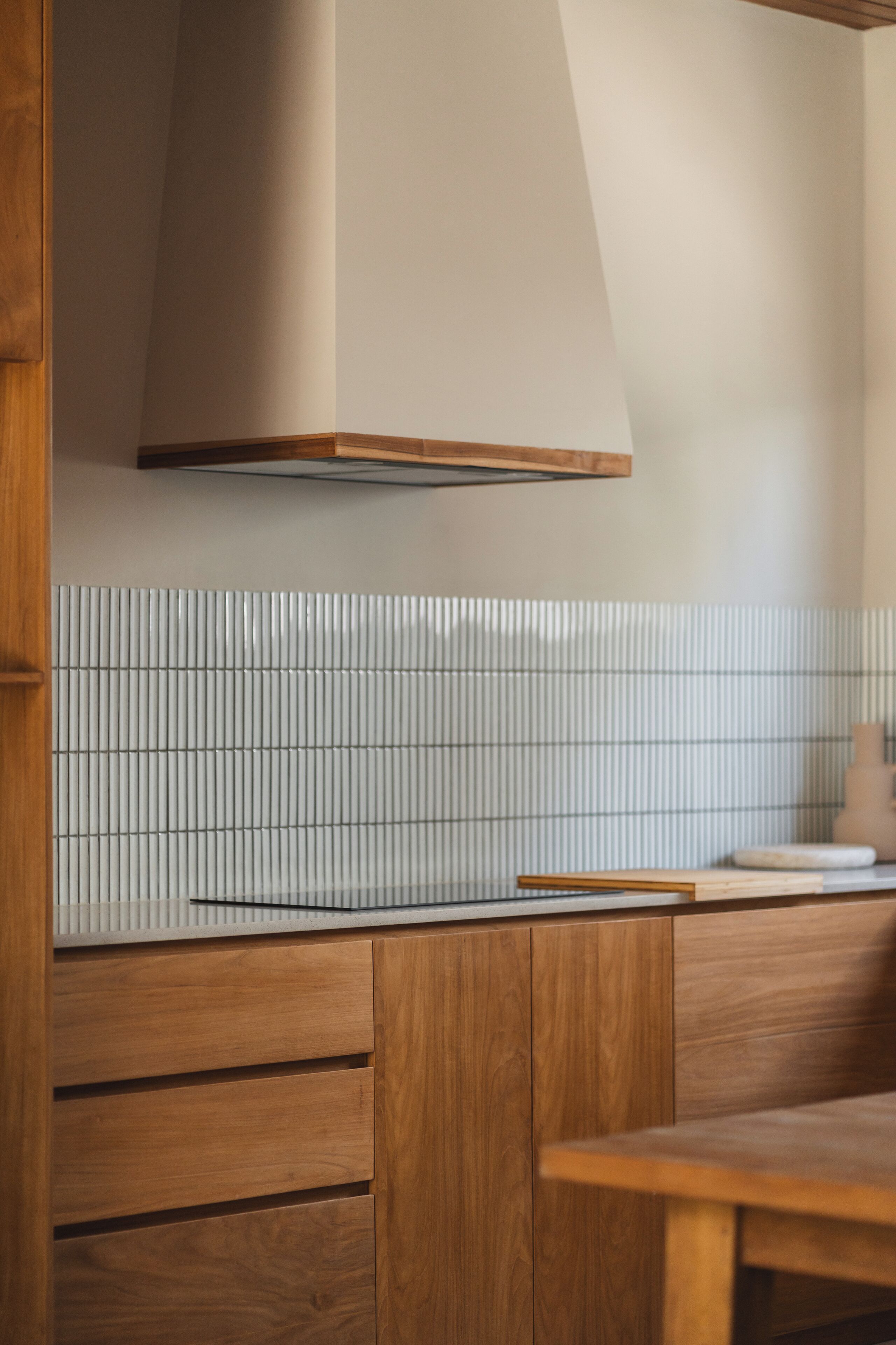 A wooden bench and a table in a modern kitchen with a white tiled backsplash and a wooden cabinet.