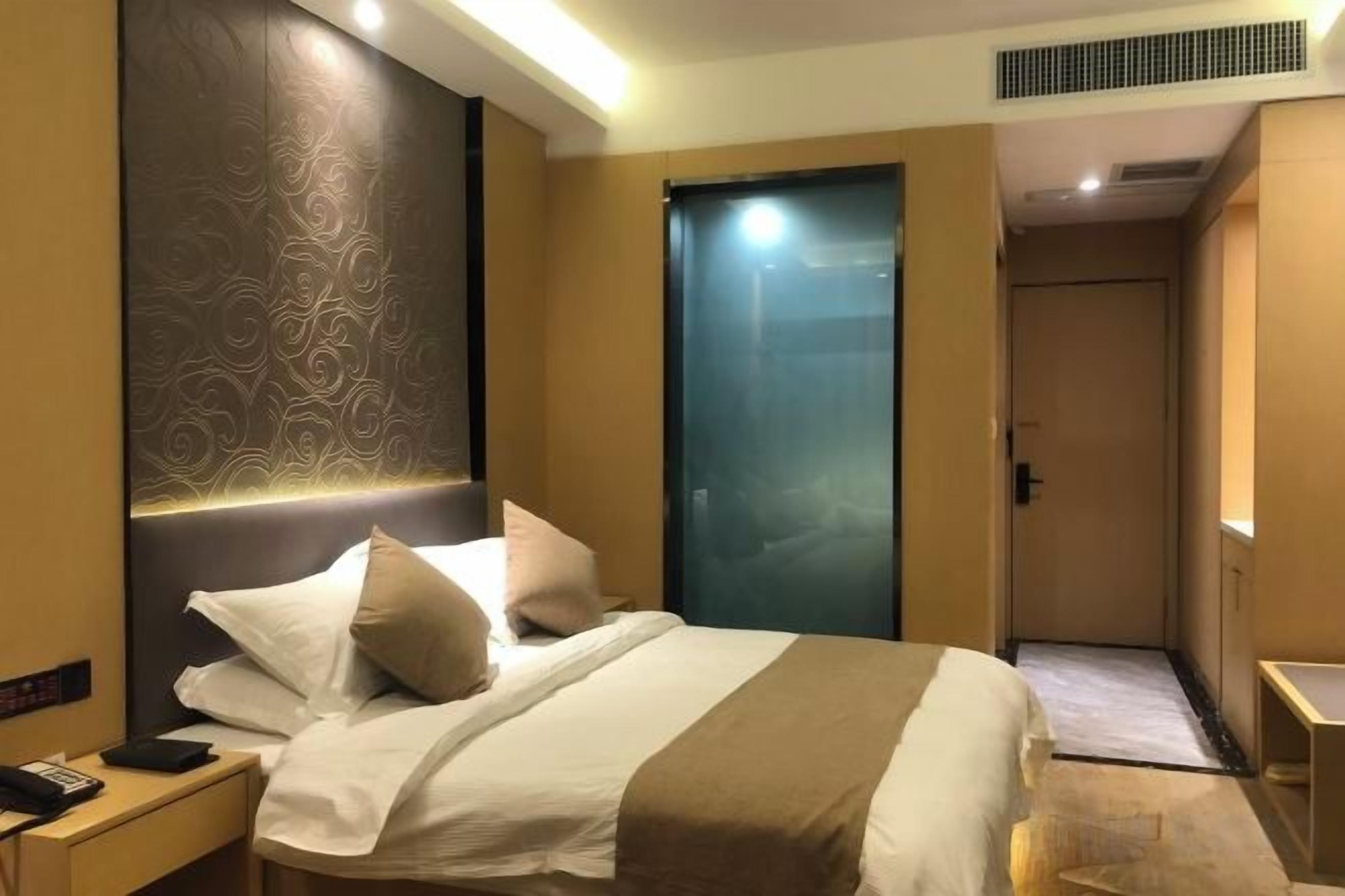 A hotel room with a bed, bedside table, and a door.