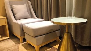 A modern hotel room with a grey upholstered sofa, a small round table with a glass top, and a wooden nightstand. - Jinyuan Hotel (Nang County)