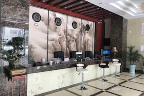 A reception area with a marble counter, multiple clocks, bar stools, a television, and a potted plant. - Jinyuan Hotel (Nang County)