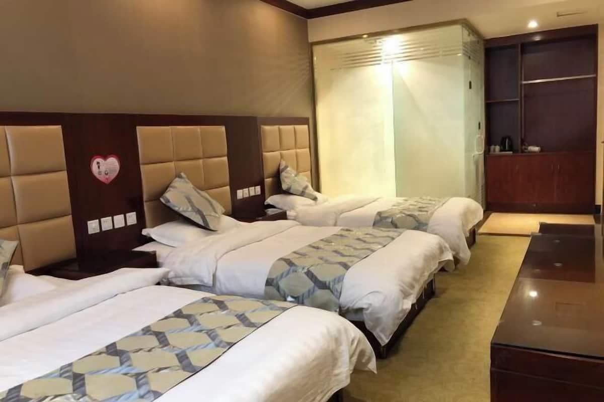 Ett hotellrum med tre sängar, en sänggavel i trä, en garderob och en hjärtformad dekoration på väggen.