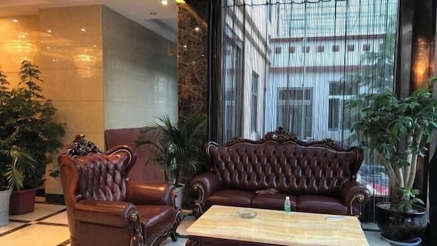 A lobby with a dark brown leather sofa and armchair, a wooden coffee table, and potted plants. - Jinyuan Hotel (Nang County)