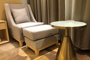 Una habitación con un sillón tapizado gris, una mesita redonda con un vaso encima y una mesita de noche de madera.