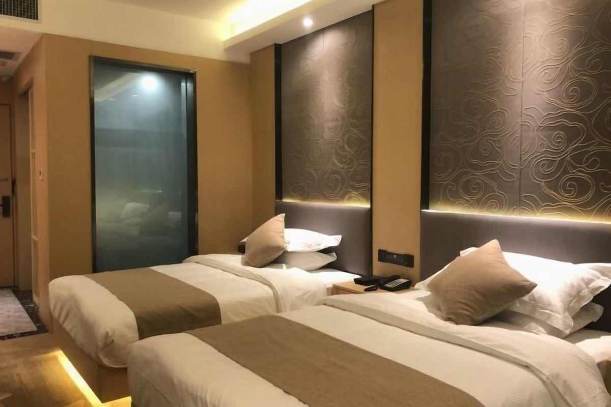 Habitación de hotel con dos camas, una puerta de vidrio y una pared con diseño texturizado.