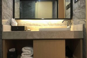 Un baño con encimera de mármol, lavabo, espejo y toallero.