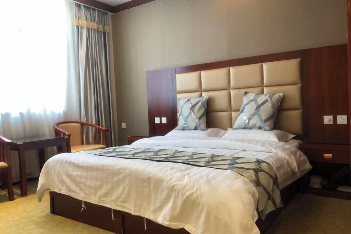 Una habitación de hotel con una cama grande, cabecera de madera, dos almohadas, una mesita de noche y una silla.