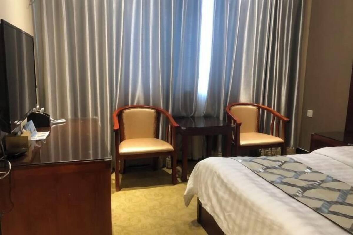 Ett hotellrum med en säng, två trästolar, ett skrivbord och en tv.