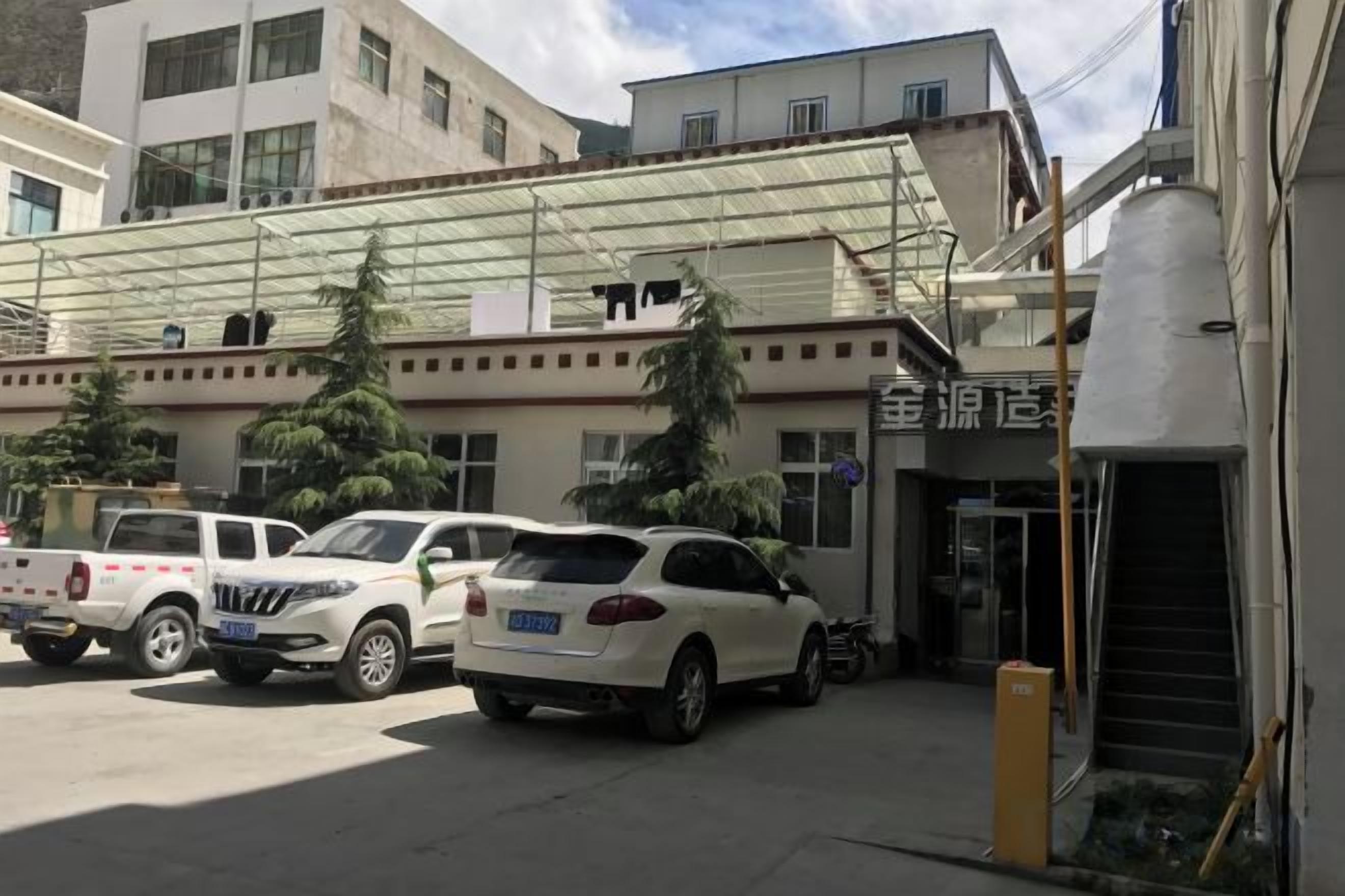 A building with a covered entrance, parked vehicles, and a staircase leading to the entrance.