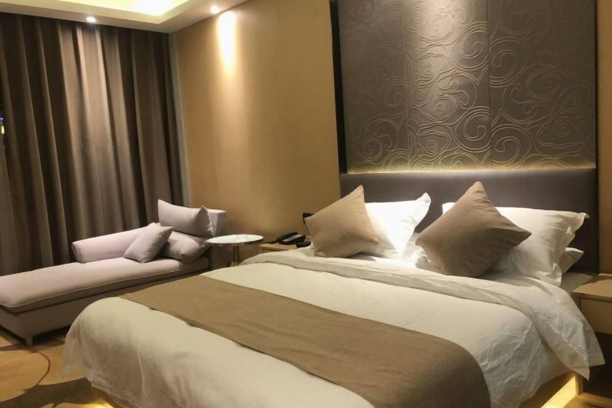 Ett hotellrum med en stor säng, en soffa, ett sängbord och en sänggavel med ett dekorativt mönster.
