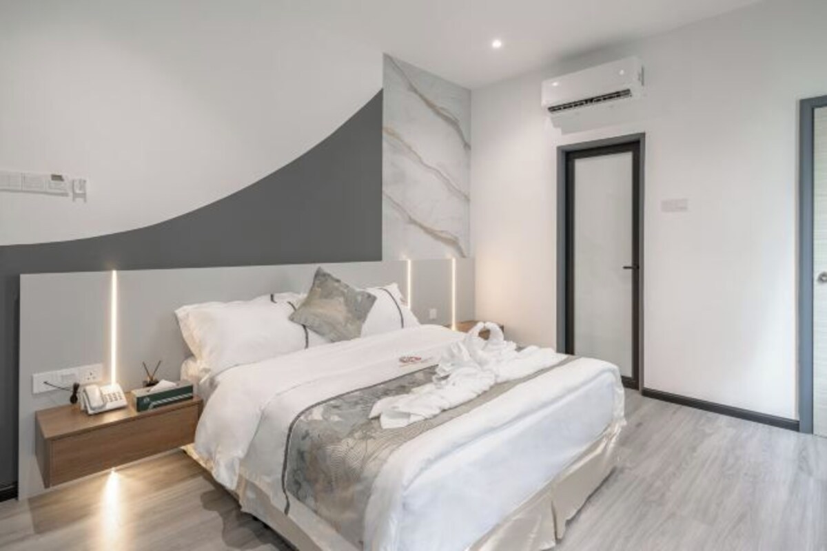 A modern bedroom with a curved headboard, a bedside table with a lamp, and a neatly made bed with a blanket and pillows.