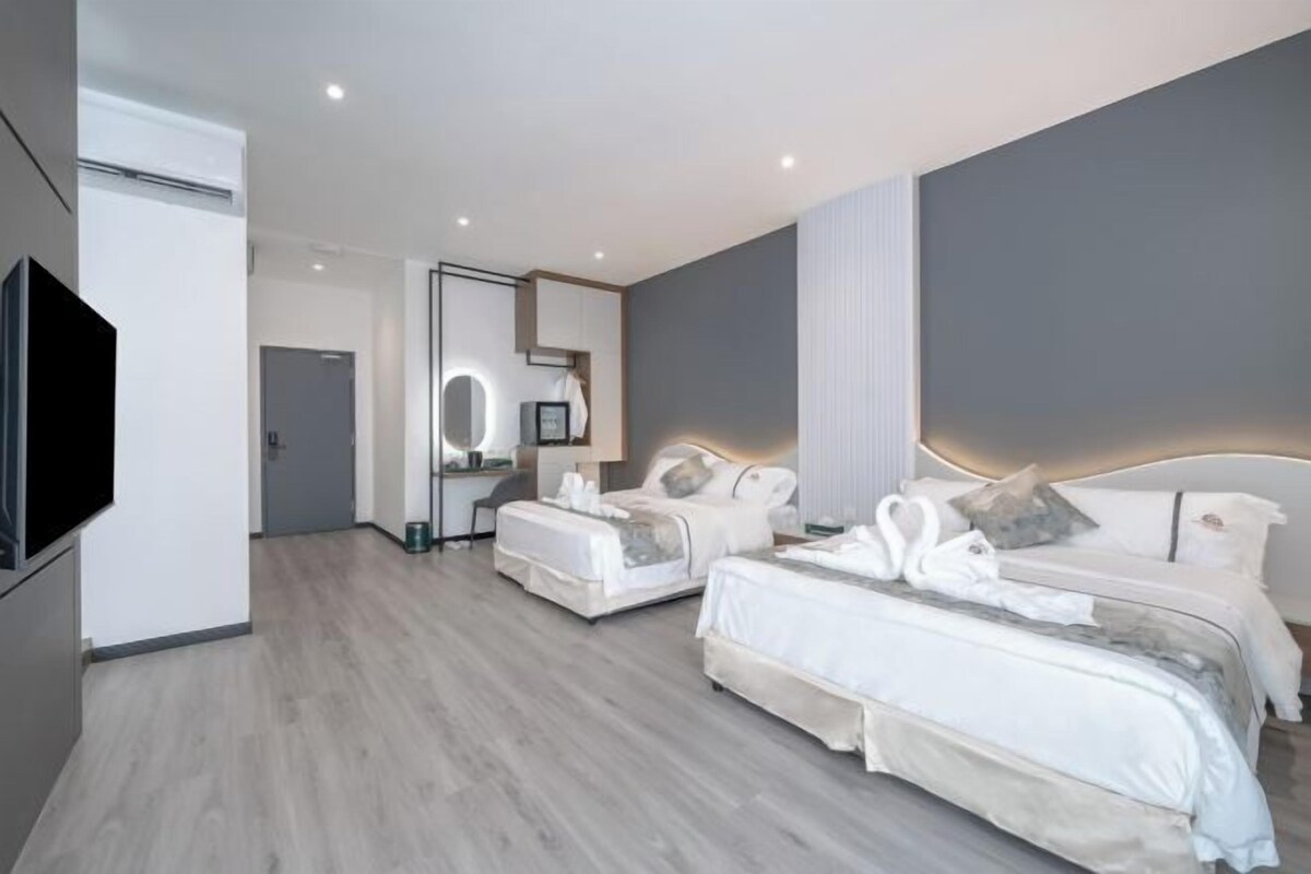Ett modernt hotellrum med två sängar, en TV, en spegel och en liten arbetsplats med skrivbord.