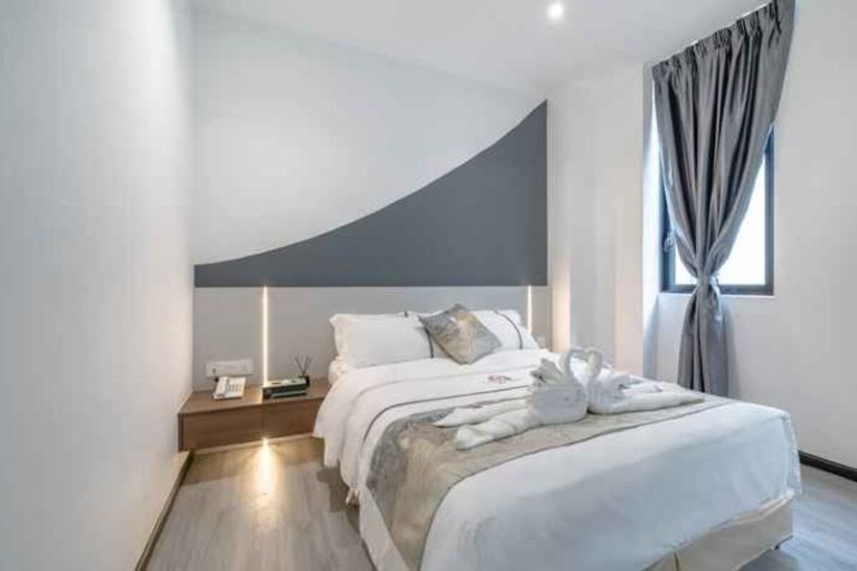 Ein modernes Schlafzimmer mit einem gewölbten Kopfteil, einem ordentlich bezogenen Bett mit weißen Leinen, einem Nachttisch mit Lampe und einem Fenster mit Vorhängen.
