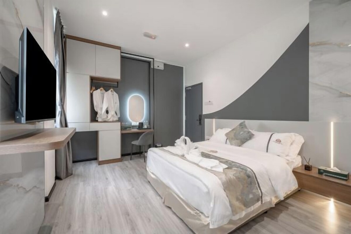 Quarto de hotel moderno com cama, mesa de cabeceira, televisão e escrivaninha com espelho.