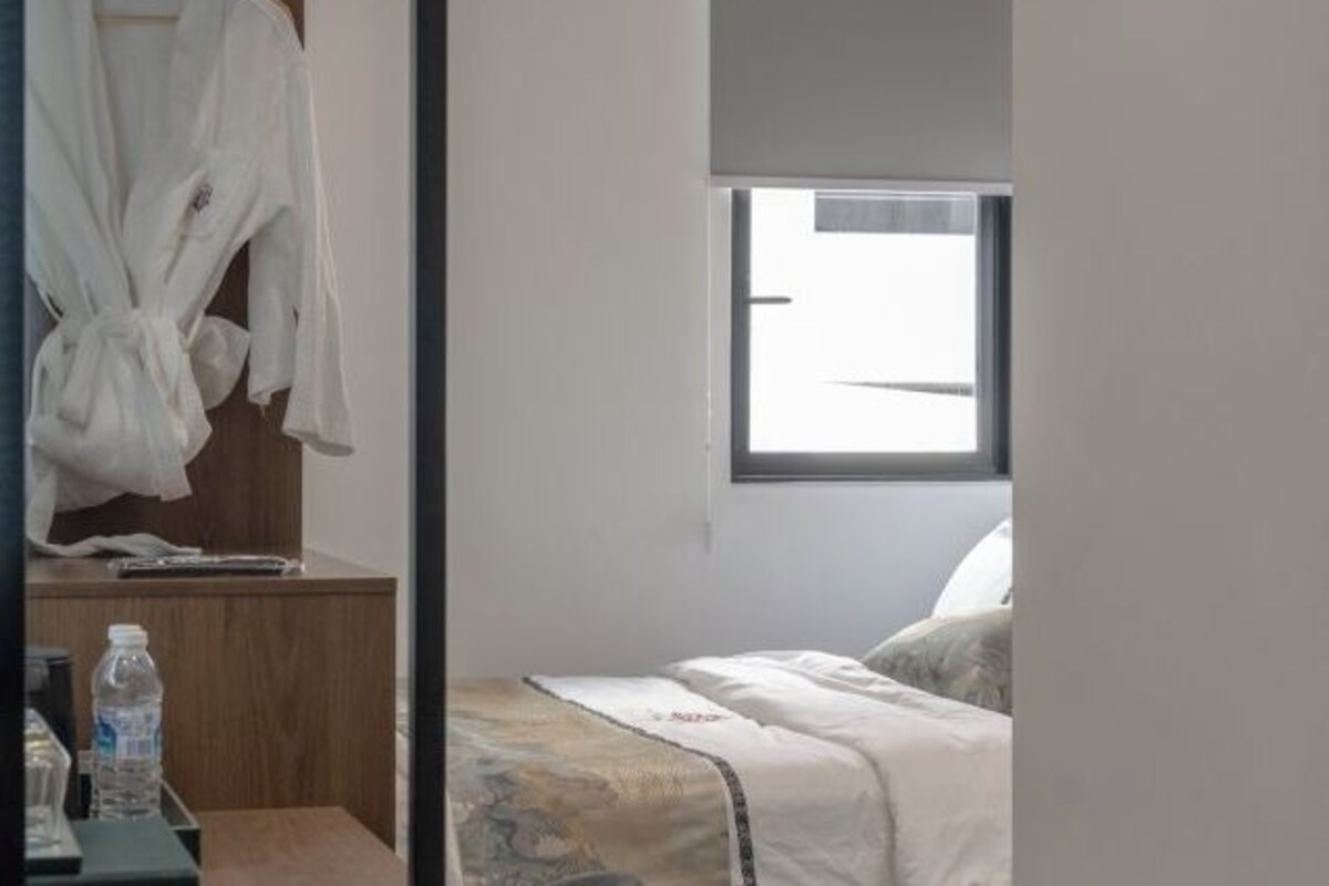 Ein Schlafzimmer mit einem Bett, einem Fenster, einem Holztisch und einem Bademantel, der an einem Haken hängt.