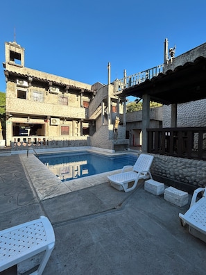 Un espace piscine avec des chaises longues et un bâtiment doté de nombreux balcons.