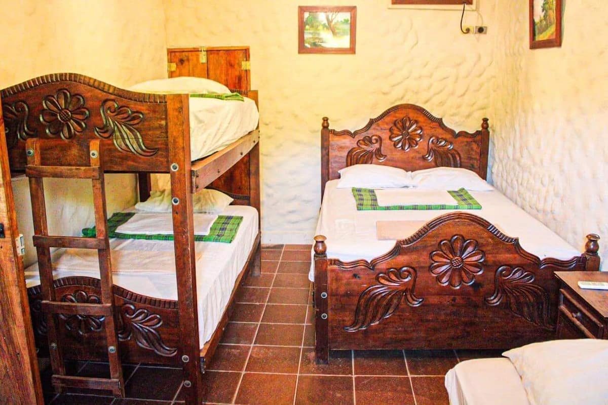 Quarto com duas camas beliches de madeira, uma mesa pequena e uma cadeira.