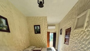 Un couloir étroit mène à deux lits simples dotés de têtes de lit, une porte en bois et une petite fenêtre avec des volets.