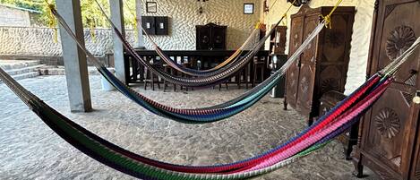 A hammock in a covered outdoor area with a stone floor, a wooden cabinet, and a chandelier.