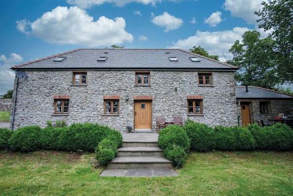 A stone house with a central entrance, multiple windows, and a small porch area.