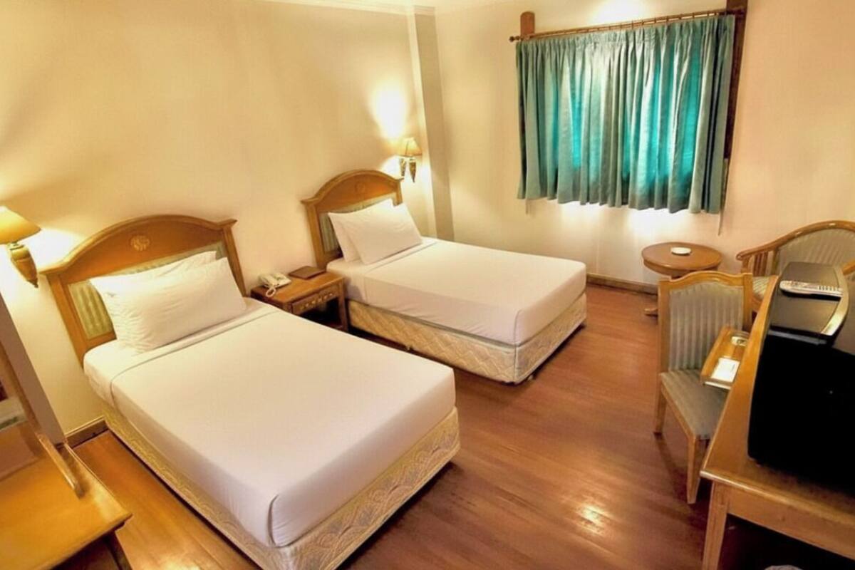 Une chambre d’hôtel avec deux lits simples, un bureau en bois avec une télévision, une petite table et une chaise.