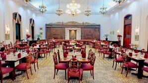 Een ruime balzaal met ronde tafels en stoelen, kroonluchters en een decoratieve achtergrond.