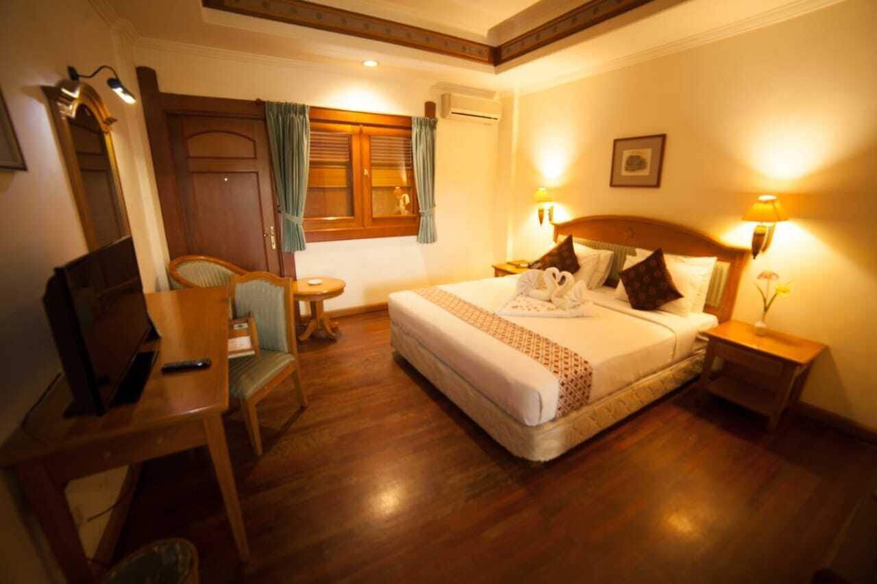 A hotel room with a bed, bedside lamps, a chair, a desk, and a window with curtains.