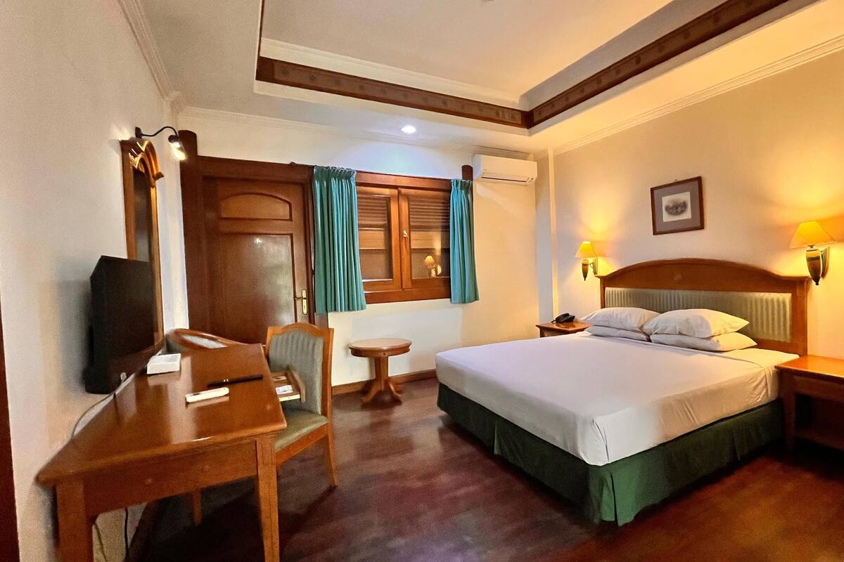 Une chambre d’hôtel comprenant un lit, des tables de chevet, un bureau avec une chaise, une télévision et une fenêtre avec des rideaux.