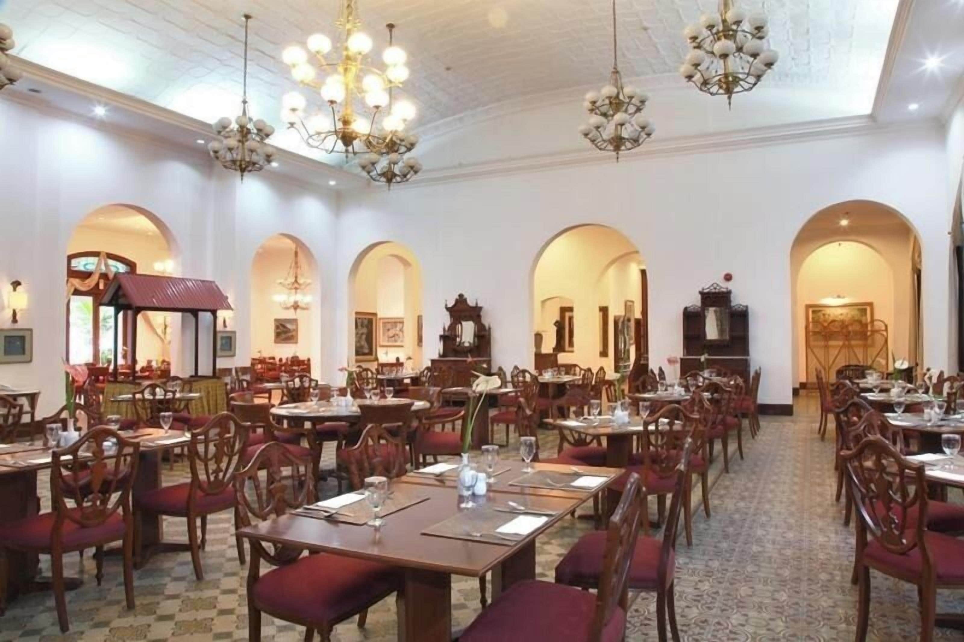 A spacious dining area with multiple tables and chairs, chandeliers, and arched doorways.