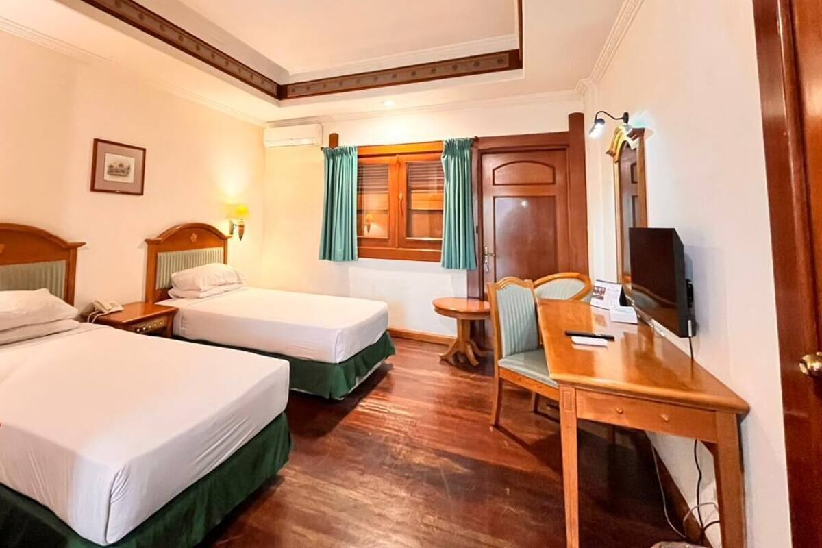 Une chambre d’hôtel avec deux lits, un bureau, une chaise, une télévision et une fenêtre avec des rideaux.