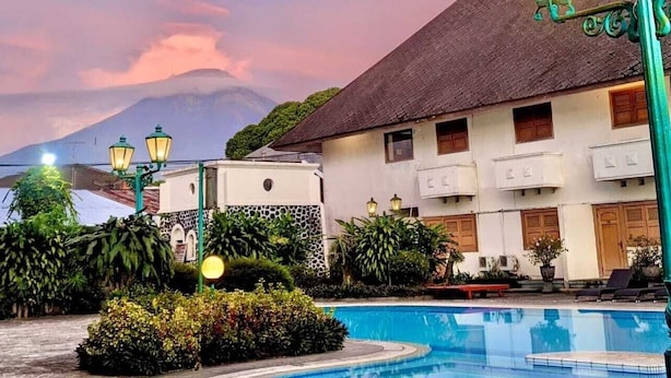 Een hotel met een zwembad, omringd door weelderige begroeiing en een berg op de achtergrond.