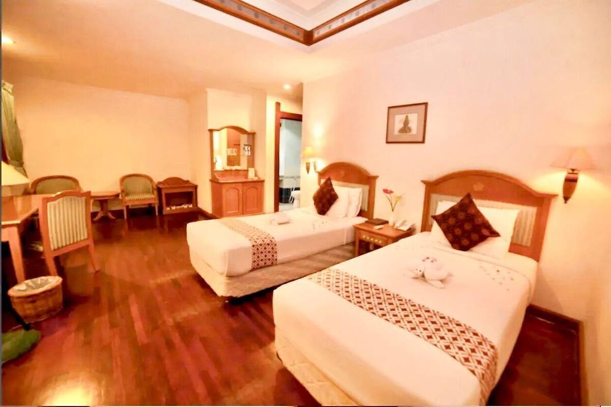Une chambre d’hôtel avec deux lits, un plancher en bois, un miroir, une petite table et une chaise.