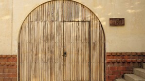 A wooden arched gate with a metal lock, set against a beige wall with a brick base. - Villa Noyollo Punta Pérula, Jalisco (Pérula)