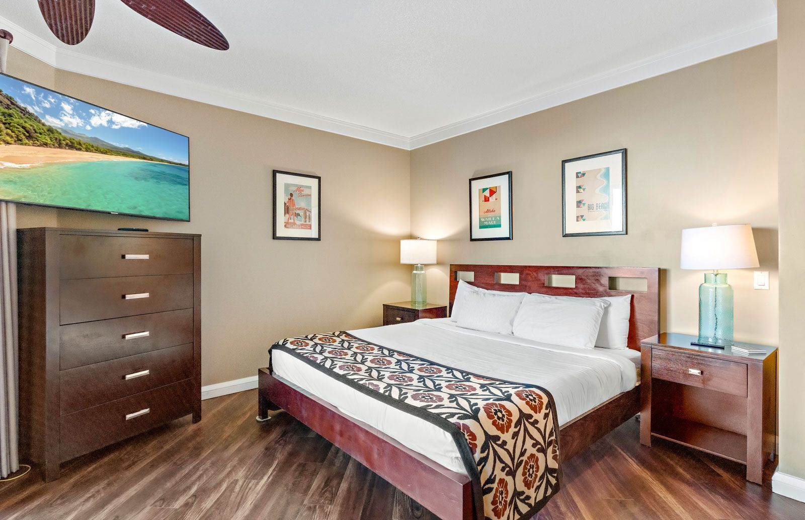A hotel room with a bed, a dresser, a nightstand, and a TV displaying a beach scene.