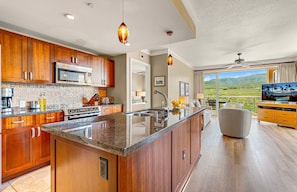 A spacious kitchen with wooden cabinets, a large island, and a view of a balcony with a scenic landscape.