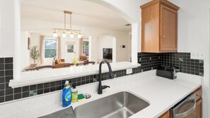 A modern kitchen with a white countertop, stainless steel sink, and wooden cabinets. - Spacious 4BR w Game Room - 15 min to Seaworld (San Antonio)