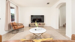 A modern living room with a sofa, a coffee table, a TV, and a staircase. - Spacious 4BR w Game Room - 15 min to Seaworld (San Antonio)