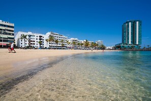 A beachside hotel with multiple floors, palm trees, and a clear blue sky. - Rosa Reducto 1 (Arrecife)