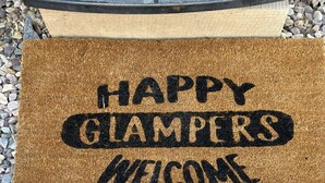 Tapete de boas-vindas com a inscrição 'HAPPY GLAMERS WELCOME' em superfície texturizada.