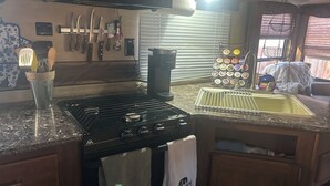 Cozinha equipada com fogão, pia e diversos utensílios. Há uma cafeteira e um suporte com recipientes.