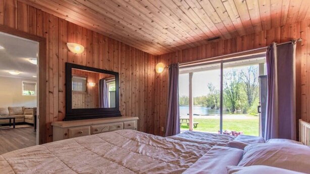Ein Schlafzimmer mit einem großen Bett, Holzwänden, einem Spiegel und Blick auf einen See.