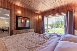 A bedroom with a large bed, wooden walls, a mirror, and a view of a lake.