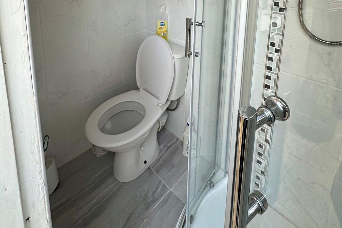Un baño con inodoro, cabina de ducha y dispensador de papel higiénico.