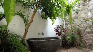 Una bañera de piedra grande rodeada de exuberante vegetación y un muro de piedra.