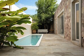 A swimming pool with a stone patio, a bench, and a tree in the background.