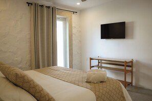 A hotel room with a bed, a TV mounted on the wall, a wooden side table, and a window with curtains.
