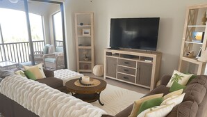 Een woonkamer met een grote bank, een salontafel, een tv op een houten dressoir en een boekenkast.