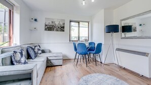 Een moderne woonkamer met een grijze bank, blauwe stoelen, een eettafel en een groot raam.