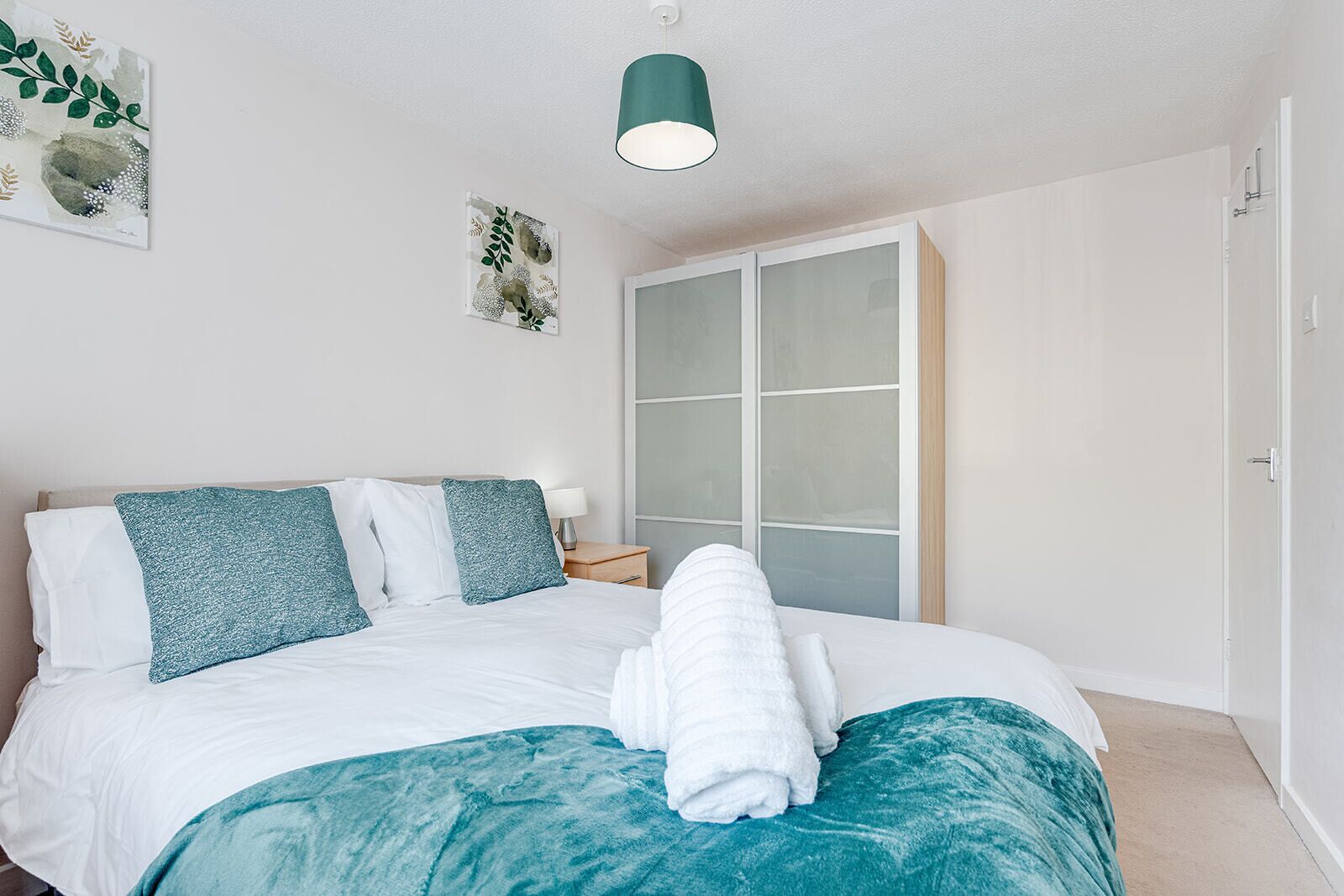 A neatly made bed with white and teal bedding, a bedside lamp, and a towel on the bed.