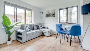 Een moderne woonkamer met een grijze modulaire bank, blauwe fauteuils, een eettafel en grote ramen met uitzicht op de stad.