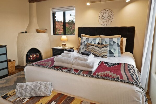 A bedroom with a bed, a fireplace, a nightstand, and a window with a view.